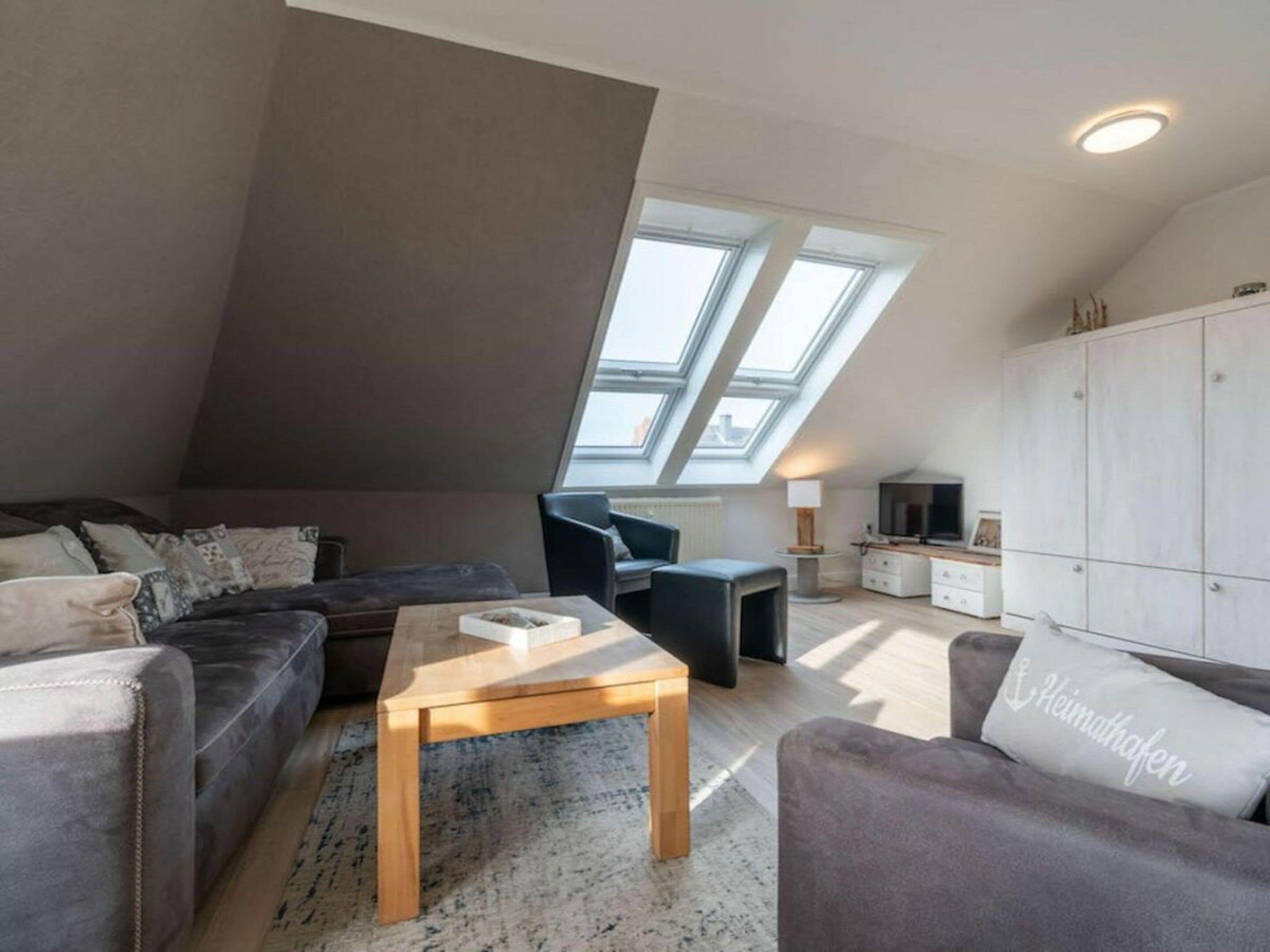 Ett modernt vardagsrum i loftstil med ett sluttande tak, en soffgrupp, ett soffbord och en tv.