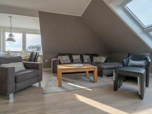 A modern loft-style living room with a sloped ceiling, a sofa set, a coffee table, and a view through a skylight. - Utholm 9 - Sea View (St. Peter-Ording)