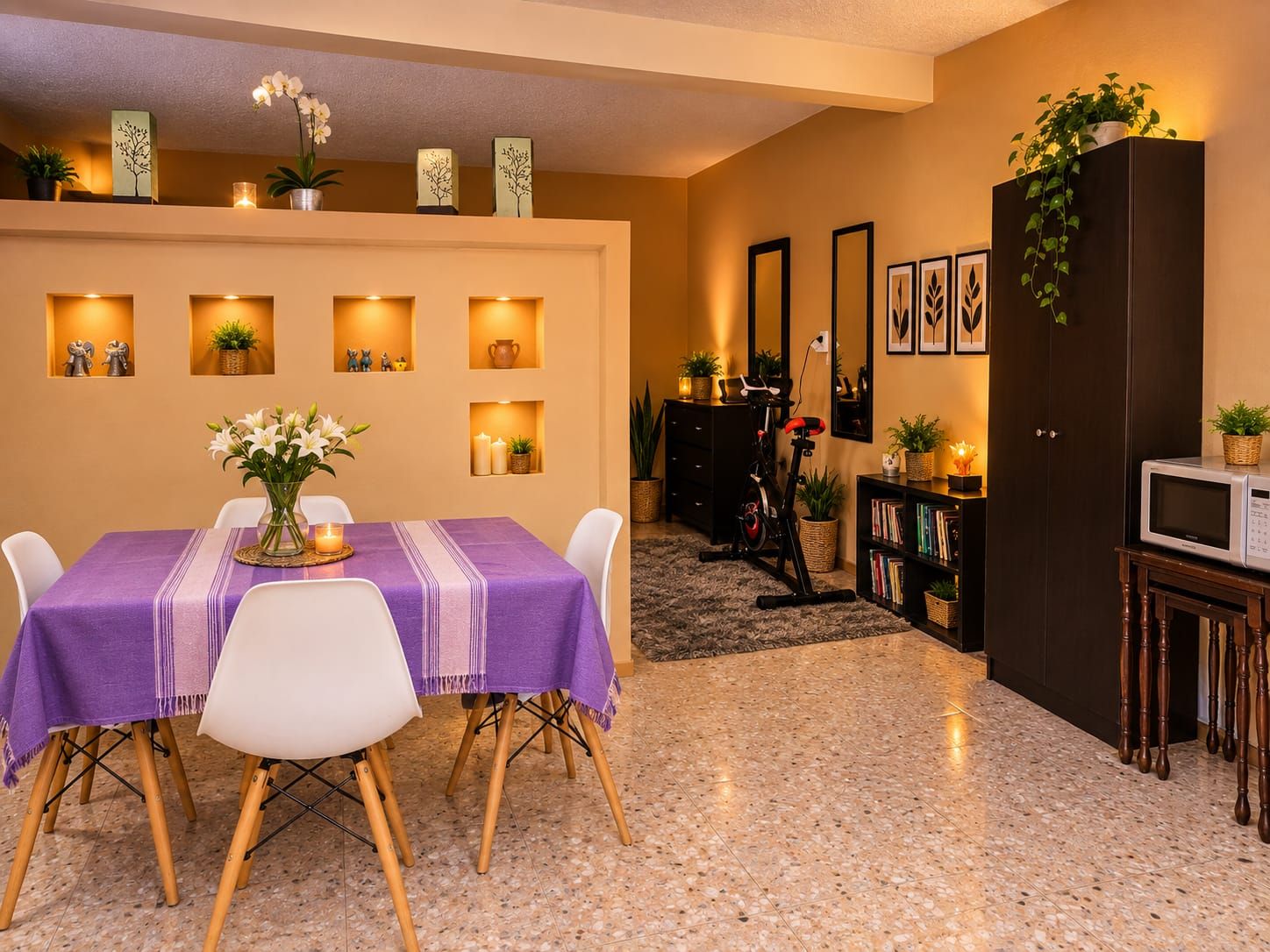 A dining area with a table set for two, a kitchen area with a microwave and bookshelves, and a living space with a sofa and a TV.