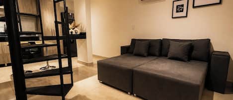 A modern living room with a sofa, a black shelving unit, and an air conditioning unit.