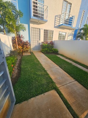 Un patio con un césped cuidado, un sendero de concreto y un edificio con múltiples ventanas y balcones.