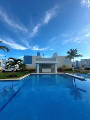 Piscina com um edifício moderno ao fundo, rodeada por palmeiras.