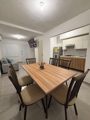 Eine moderne Küche mit Essbereich, inklusive einem Holztisch und Stühlen, einem eingebauten Ofen und einem an der Wand befestigten Fernseher.