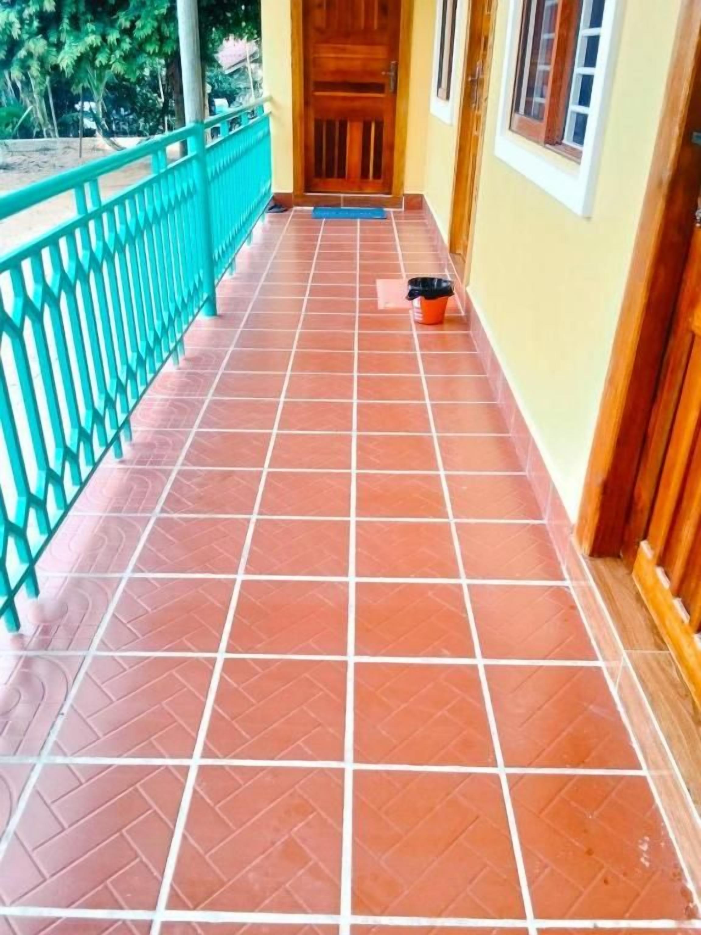 Um corredor com chão de azulejos, porta de madeira e corrimão azul.