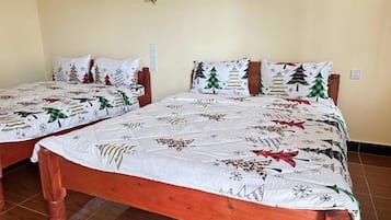 Deux lits en bois, recouverts de draps blancs ornés de motifs représentant des sapins de Noël et des flocons de neige.