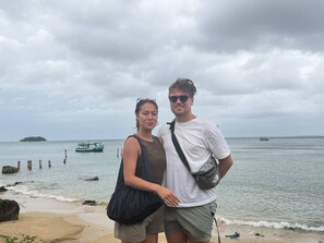 A beach with a boat in the background and a person standing on the shore.