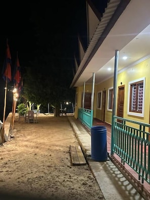 A building with a covered porch, a blue trash bin, and a wooden bench.