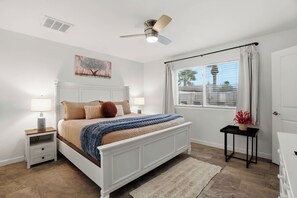A bedroom with a bed, nightstands, a ceiling fan, a window with curtains, and a painting on the wall. - Modern Paradise Retreat Pool & Outdoor Dining (Phoenix)