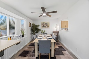 A modern kitchen with a dining area, a ceiling fan, and a window with blinds. - Modern Paradise Retreat Pool & Outdoor Dining (Phoenix)