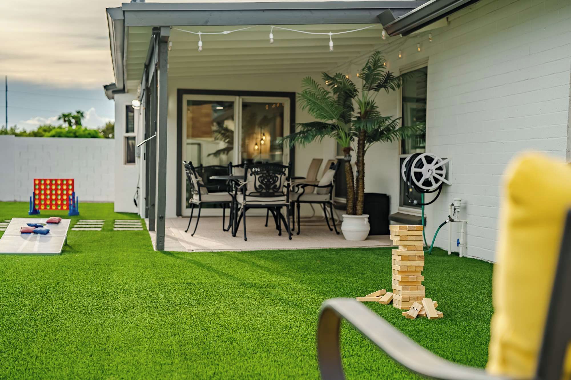 Un área de patio con una mesa y sillas, un pequeño jardín con césped artificial y una pila de bloques de madera.