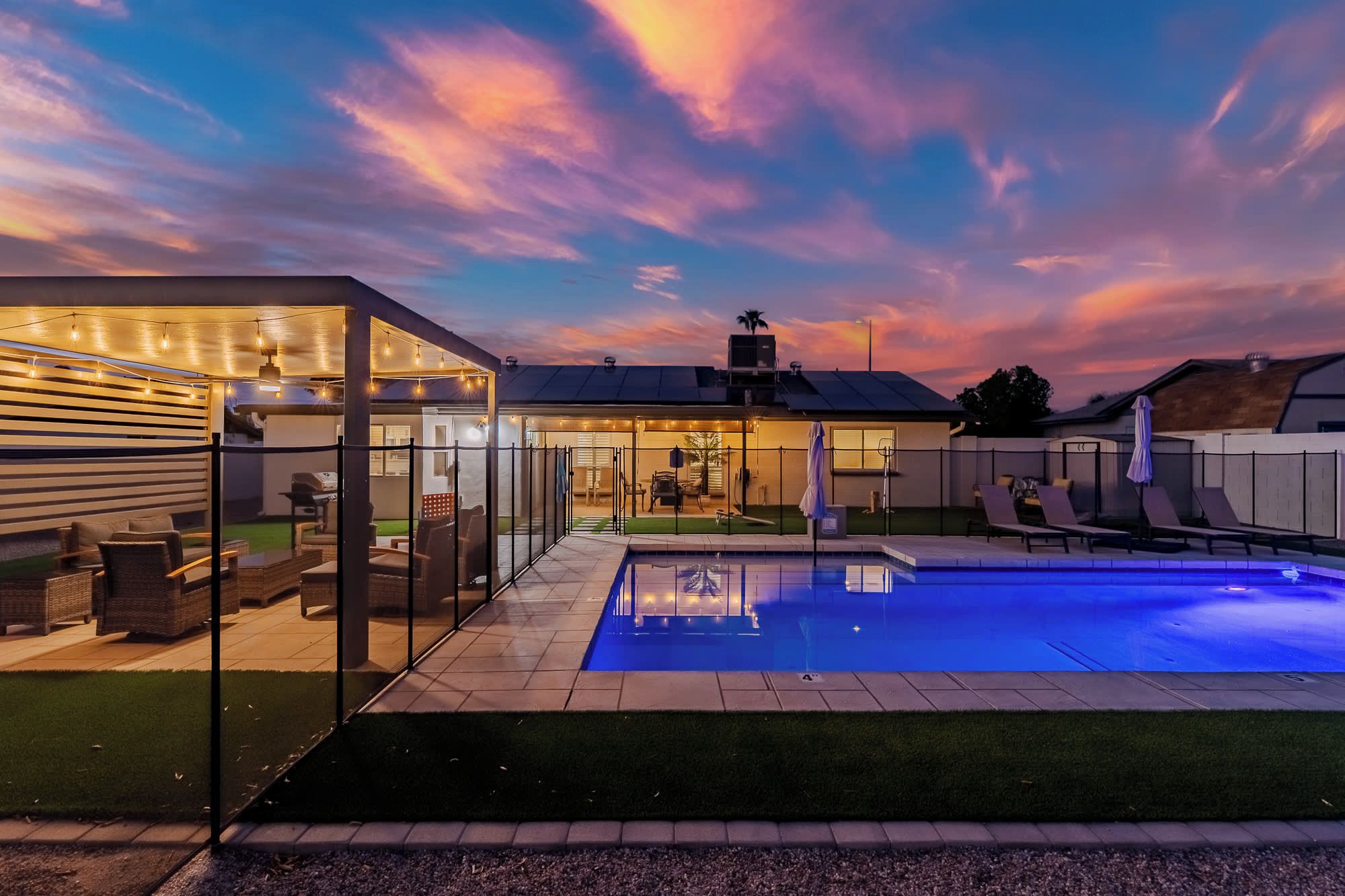 A modern outdoor pool area with a glass enclosure, lounge chairs, and a well-lit patio.