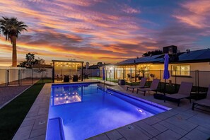 A swimming pool with a patio area, a covered seating area, and a view of the sunset. - Modern Paradise Retreat Pool & Outdoor Dining (Phoenix)