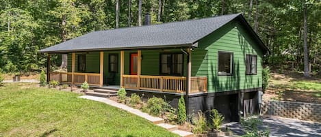 A two-story house with a green exterior, a wooden porch, and a red door.