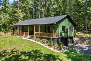 Une maison à deux étages, avec une façade verte, un porche en bois et une porte rouge.