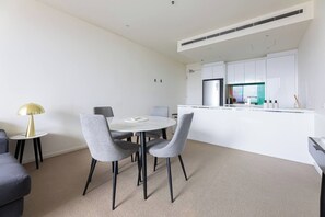 A modern kitchen with white cabinets, a dining area with a round table and grey chairs, and a small side table with a lamp. - Light Elevated Living near Queen Victoria Market (Melbourne)