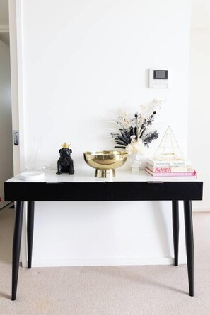 A white table with a black base, a gold bowl, a black dog figurine, a glass vase with white flowers, a golden pyramid, and a book titled 'MOVIDA'. - Light Elevated Living near Queen Victoria Market (Melbourne)