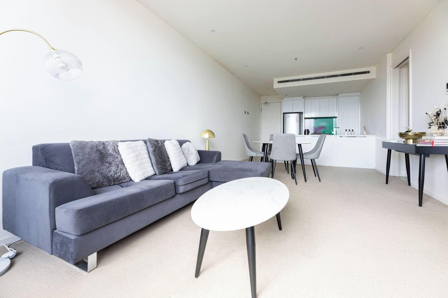 Ein modernes Wohnzimmer mit einem grauen Sofa, einem kleinen weißen Tisch und einem Essbereich mit Stühlen.
