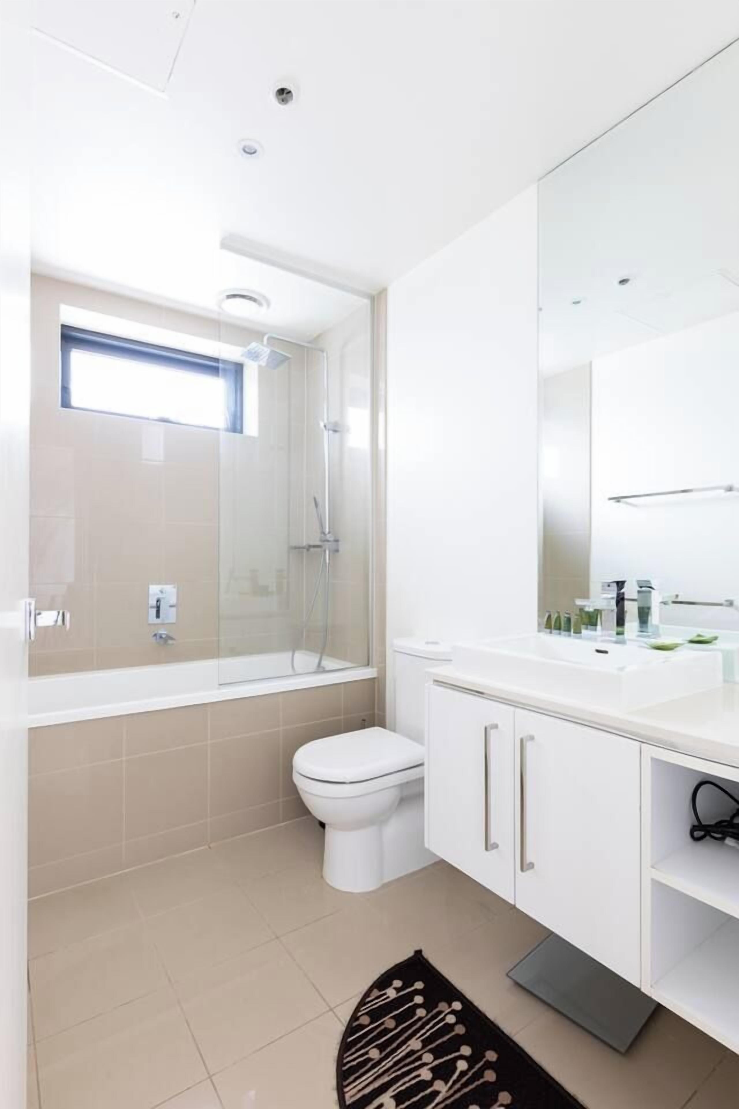 Een moderne badkamer met een douchecabine van glas, een wit toilet en een grote spiegel boven een witte wastafel.