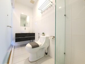 A modern bathroom with a toilet, a sink, and a glass shower enclosure. - The Wave Residence (Malacca)