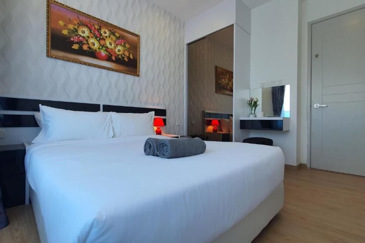 A hotel room with a large bed, a painting on the wall, a bedside table with a lamp, and a door.