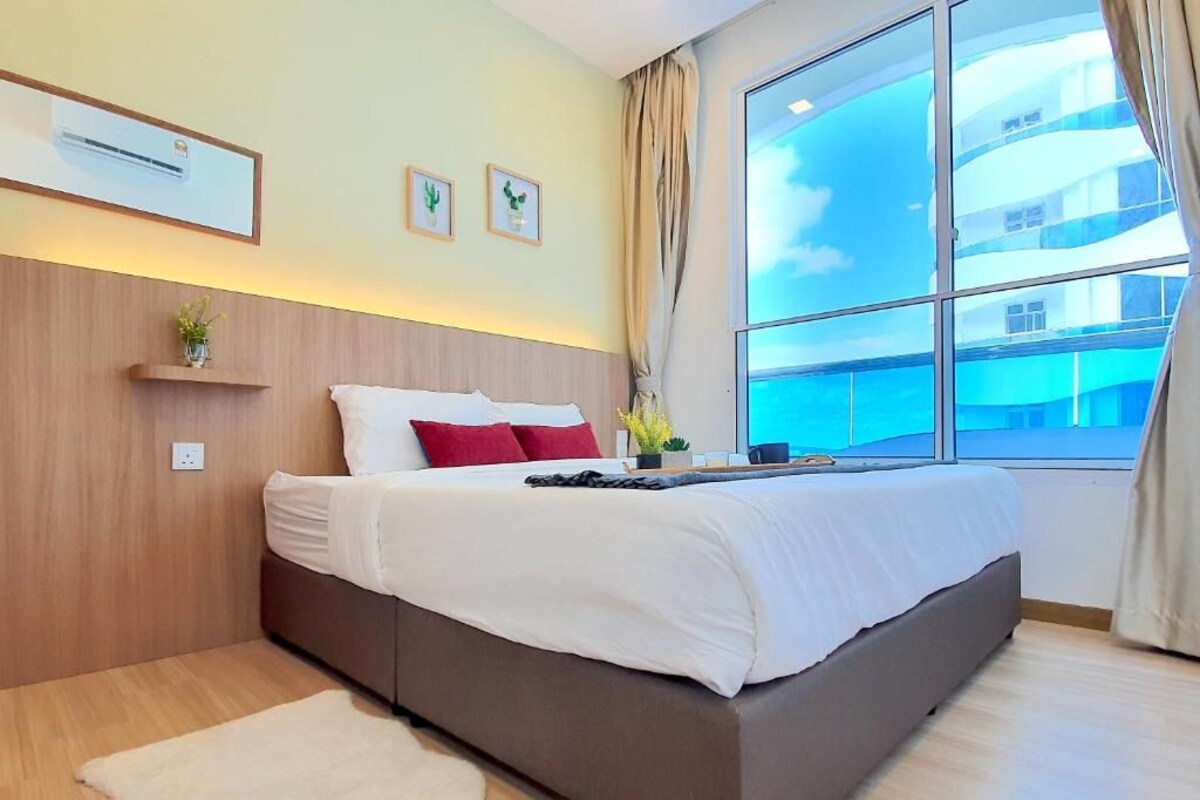 A hotel room with a large window, a bed with white bedding, a wooden headboard, and a small shelf with a plant.