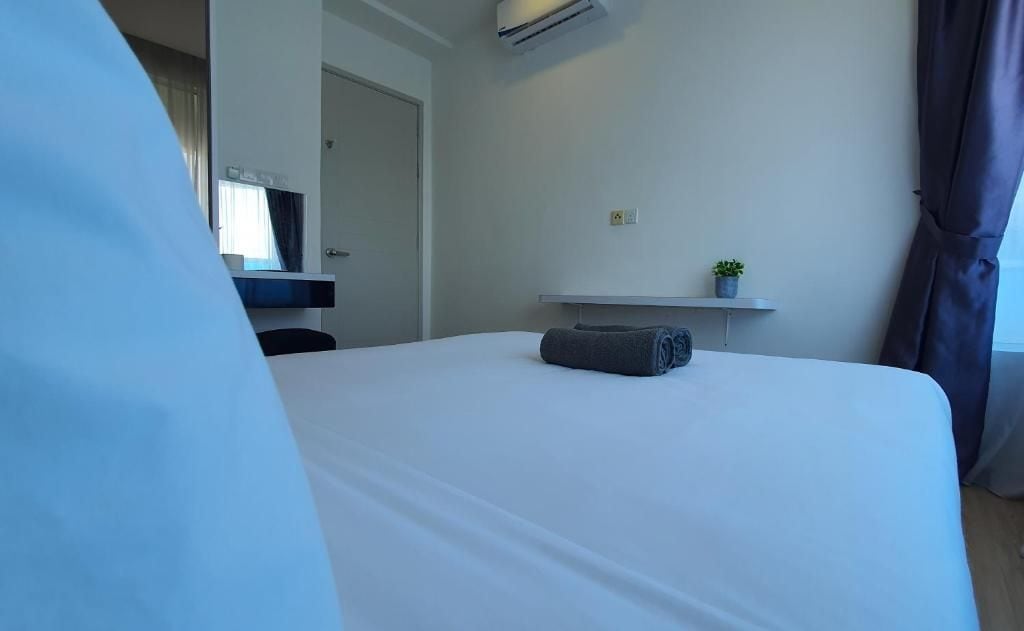 A hotel room with a bed, a small shelf with a plant, and an air conditioning unit.