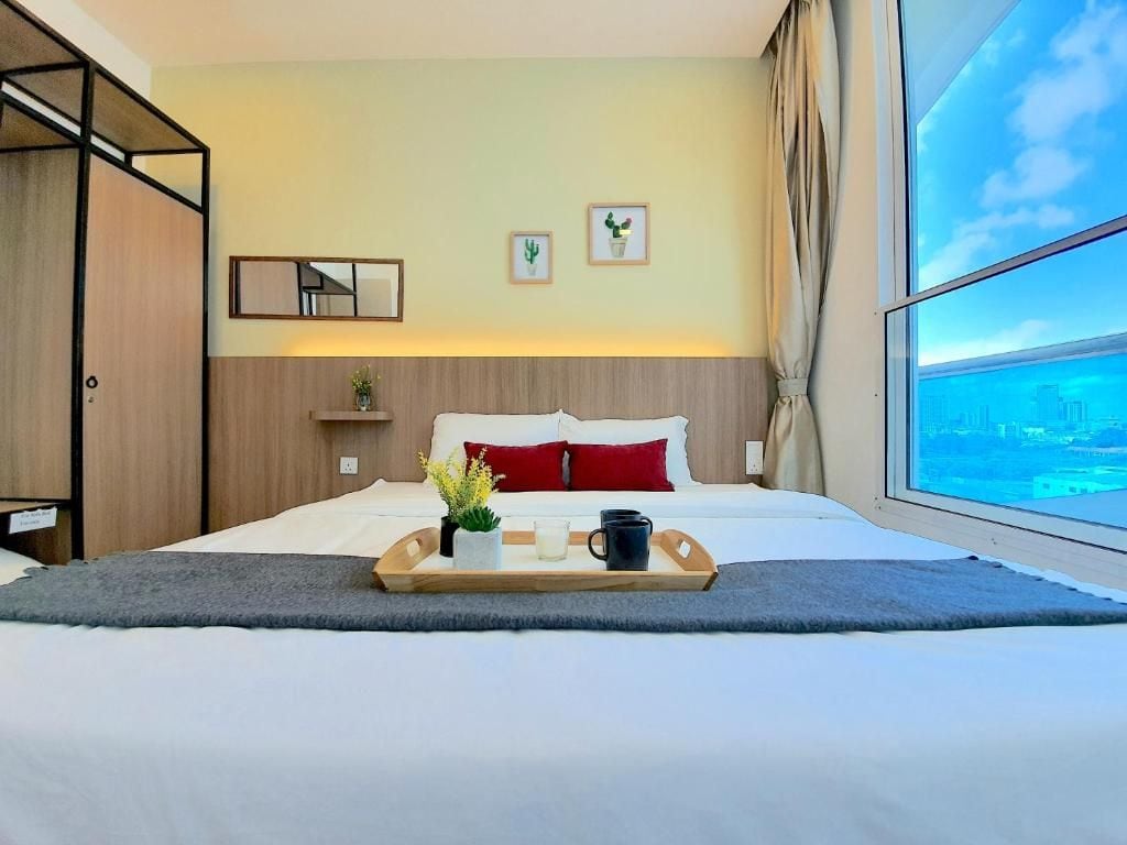 Une chambre d’hôtel avec un lit, un plateau avec une plante et une tasse, une vue sur la ville et une fenêtre avec des rideaux.