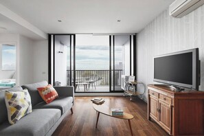 En moderne stue med en grå sofa, et fladskærms-tv, et lille sofabord og en balkon med udsigt.