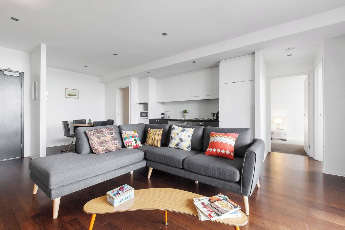Een moderne woonkamer met een grijze modulaire bank, een houten salontafel en een keuken op de achtergrond.