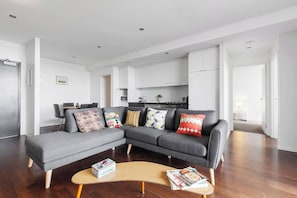 A modern living room with a grey sectional sofa, a wooden coffee table, and a kitchen in the background. - Urban Oasis in the Heart of Richmond Cultural Hub (Richmond)