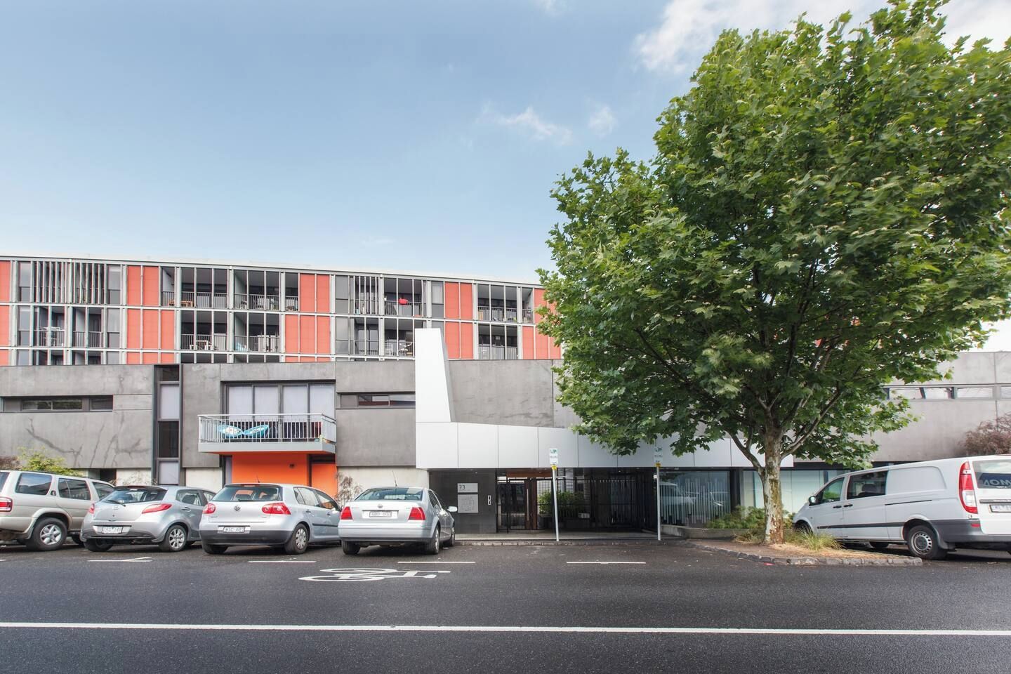 A modern building with a parking lot, a tree, and several cars.