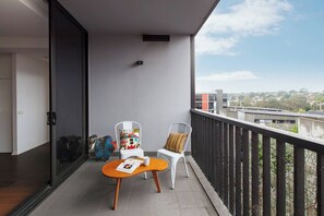 Un balcon donnant sur des immeubles, une table avec un magazine et deux chaises avec des coussins.