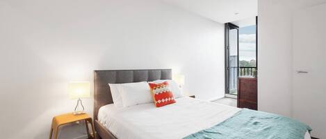 Een moderne slaapkamer met een bed, nachtlampjes, een klein houten nachtkastje en uitzicht door een groot raam.
