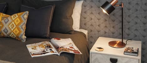 A neatly made bed with a magazine, a lamp, and a book on a bedside table.
