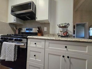 Una cocina con armarios blancos, una estufa de acero inoxidable y un microondas encima.