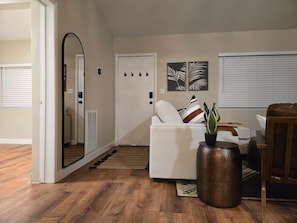 A living room with a white sofa, a large mirror, a potted plant, and a door with a light switch. - Central Oasis w/Office & Blazing Fast Wi-Fi! (San Diego)