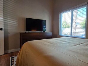 Ein Schlafzimmer mit einem Bett, einem Fernseher auf einer Kommode und einem Fenster mit Jalousien.