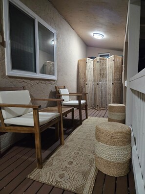 Eine Holzterrasse mit zwei weißen Polsterstühlen, einem gewebten Teppich und einem dekorativen Sichtschutz.