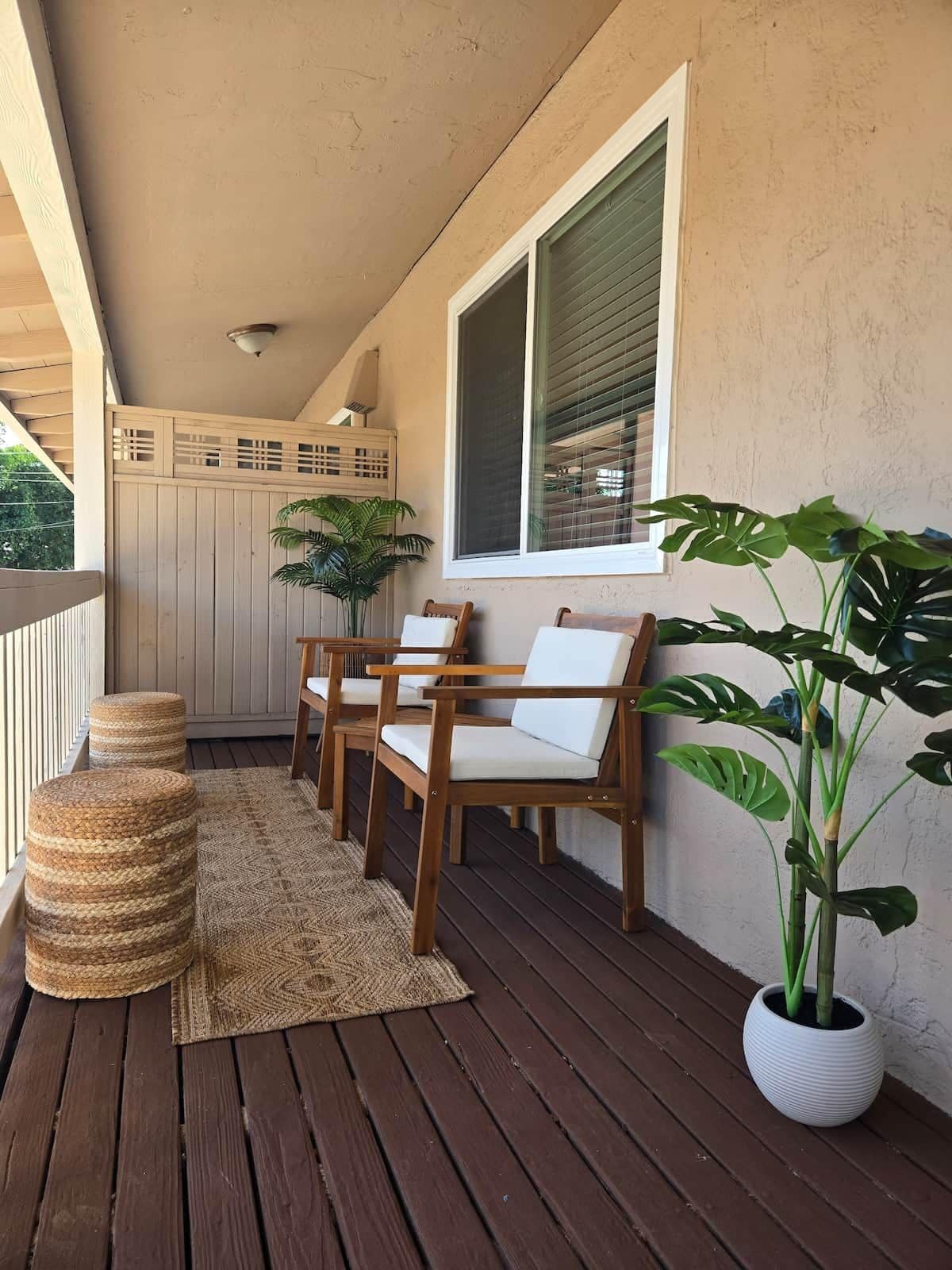 A wooden deck with a railing, a potted plant, and two chairs with cushions.