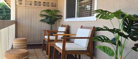 A wooden deck with a railing, a potted plant, and two chairs with cushions.