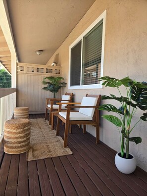 Eine Holzterrasse mit Geländer, einem Blumentopf und zwei Stühlen mit Kissen.