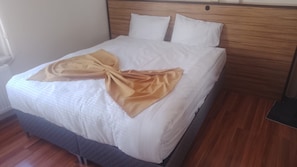 A bed with a wooden headboard, white bedding, and a folded beige blanket.