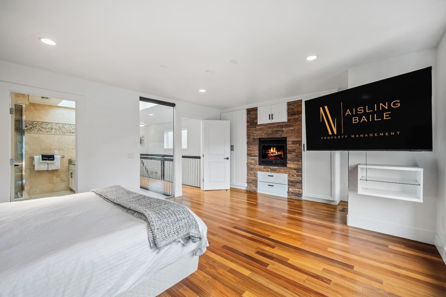 Quarto moderno com cama, lareira e televisão montada exibindo 'Aisling Baile Property Management'.