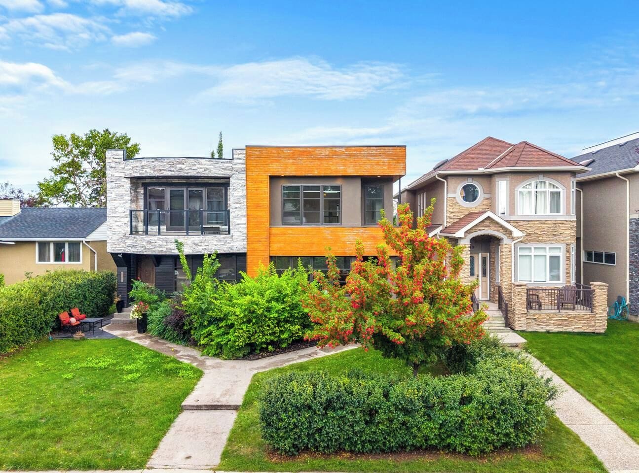 A modern two-story house with a stone facade, a wooden front section, and a well-maintained garden with various shrubs and a tree.