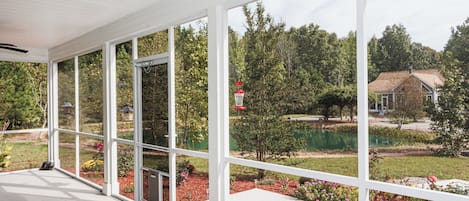 A covered outdoor area with large windows, a ceiling fan, and a small table.