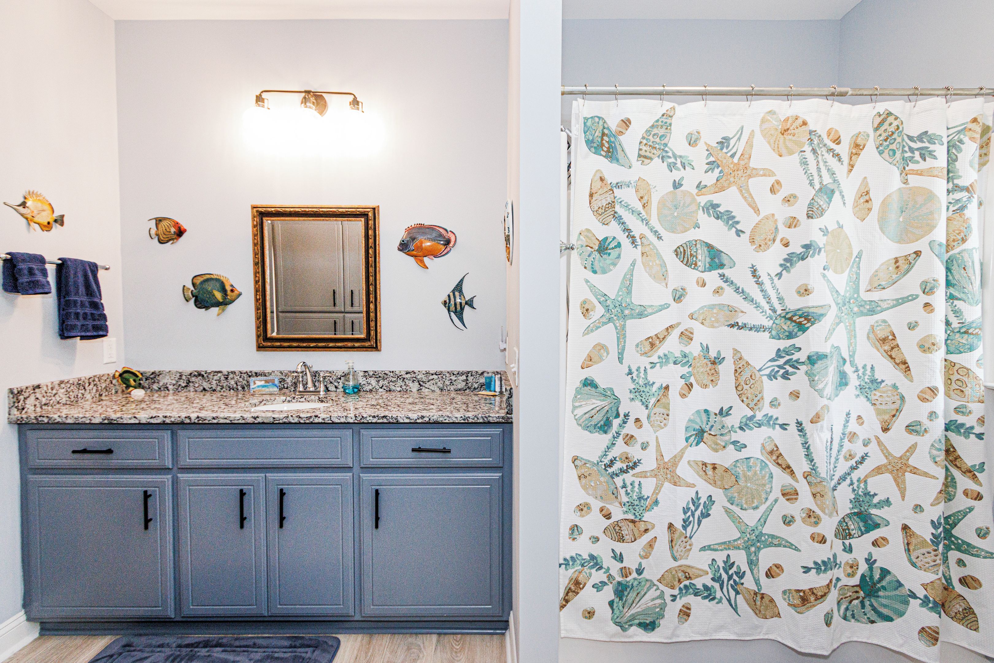 A bathroom with a granite countertop, a mirror, and a shower curtain with a sea-themed pattern.