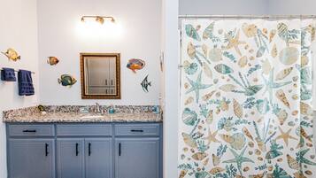 A bathroom with a granite countertop, a mirror, and a shower curtain with a sea-themed pattern.