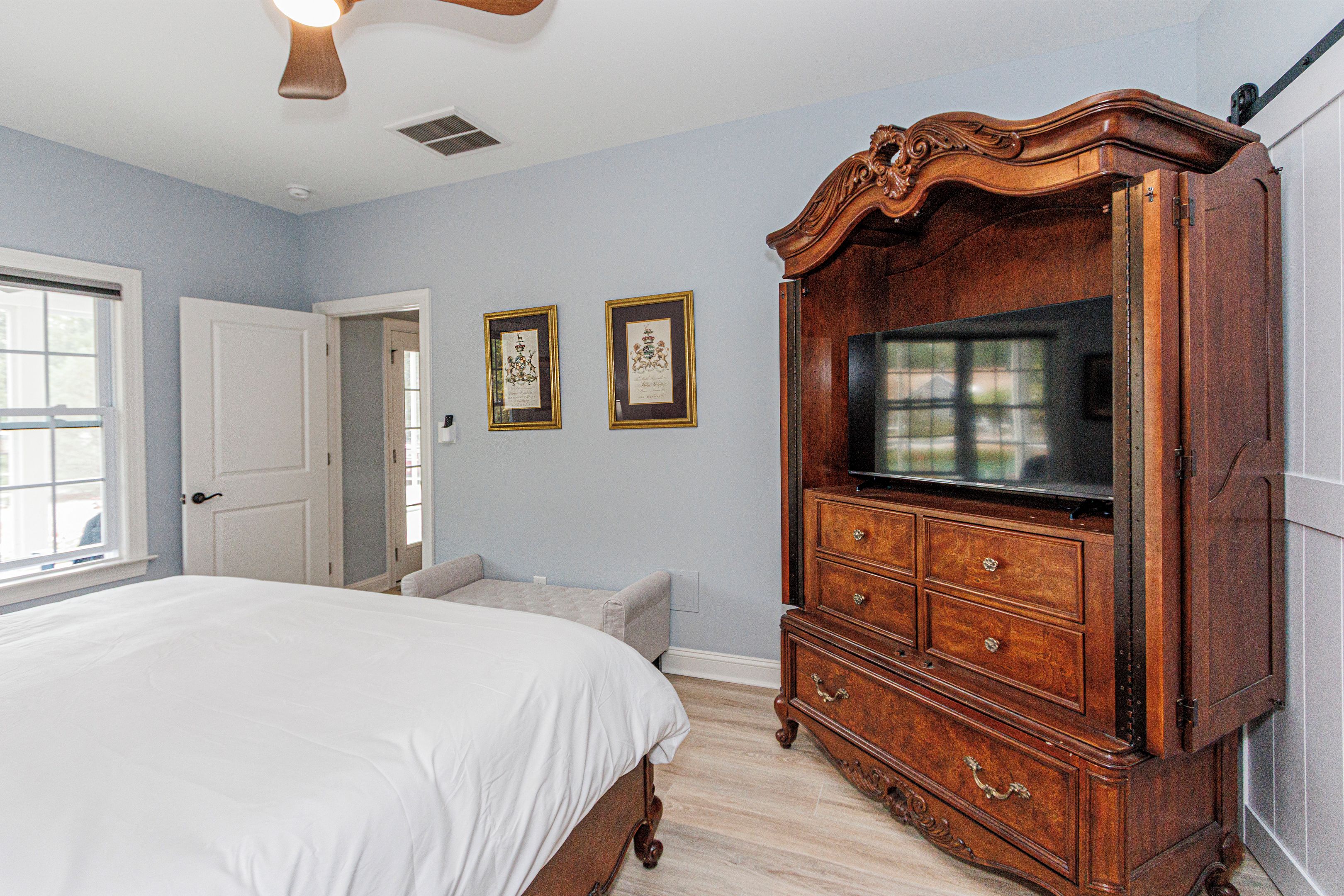 A bedroom with a large bed, a wooden dresser with a television, and two framed pictures on the wall.