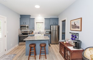 A kitchen with blue cabinets, a stainless steel refrigerator, a microwave, and a stove. There are two wooden stools at the island.
