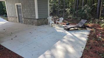 Un patio couvert avec un mur en pierre, deux chaises en plastique blanches et un fauteuil de relaxation.